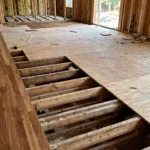 exposed plywood subfloor over floor joists next to finished hardwood flooring